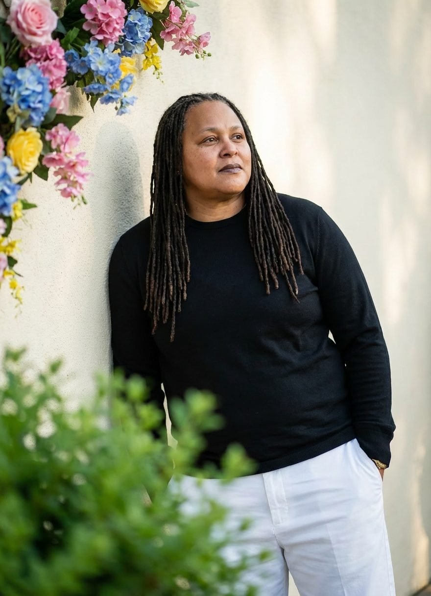 Shannon D. Hunter leaning against a sunlit wall beside flowers